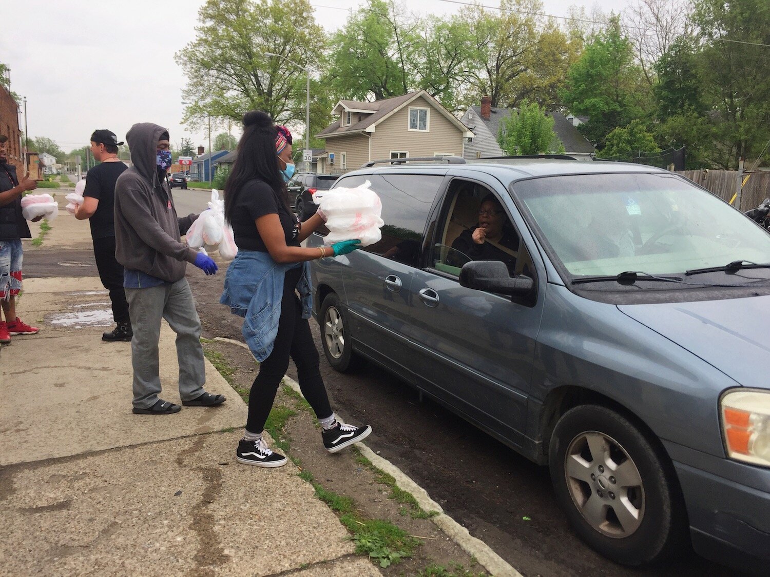 Mask-wearing volunteers deliver to-go bags to vehicles.