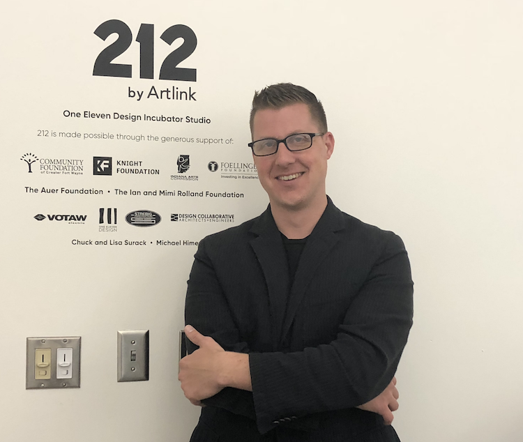 Matt McClure poses next to Artlink 212's list of sponsors.