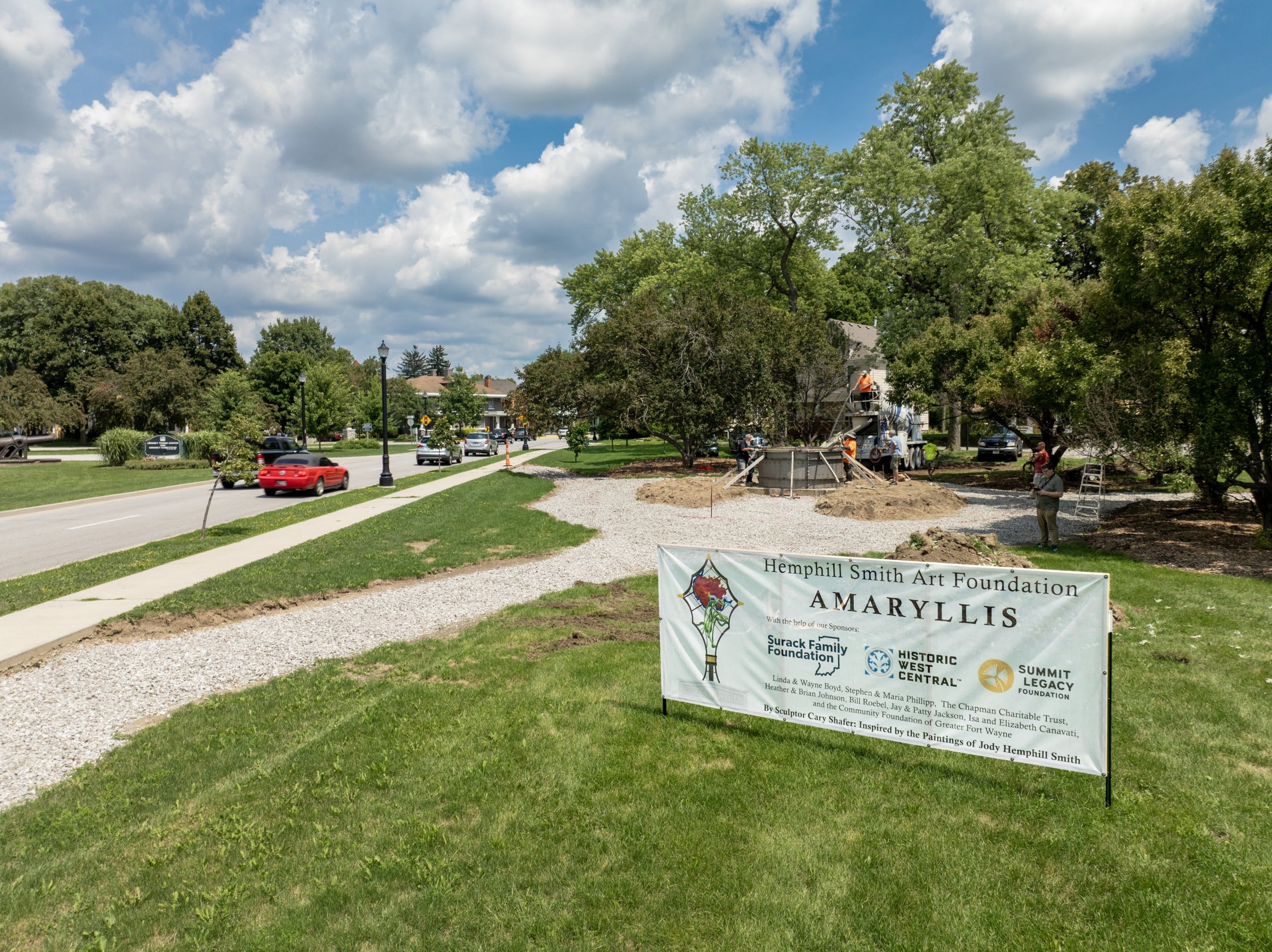 A sign reads, "Hemphill Smith Art Foundation, Amaryllis." Behind the sign, construction workers with a concrete truck work work to pour a circular base for a metal sculpture.