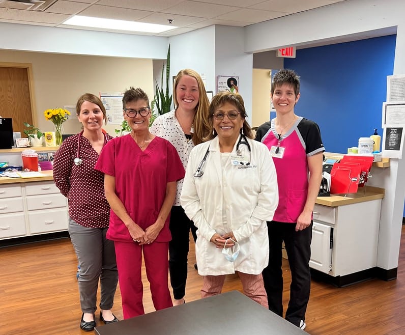 Five women in medical attire stand for a photo inside a medical office.