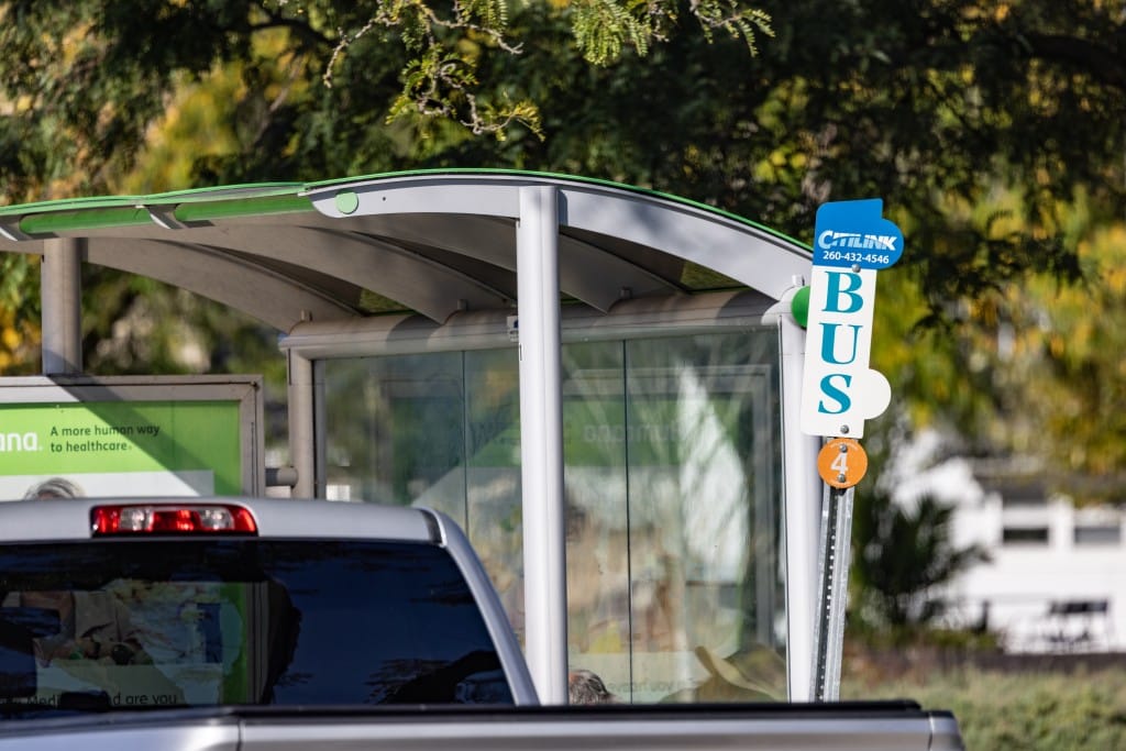 A bus shelter with three glass walls. A small sign that reads, "Citilink Bus Stop" sits in front of it.