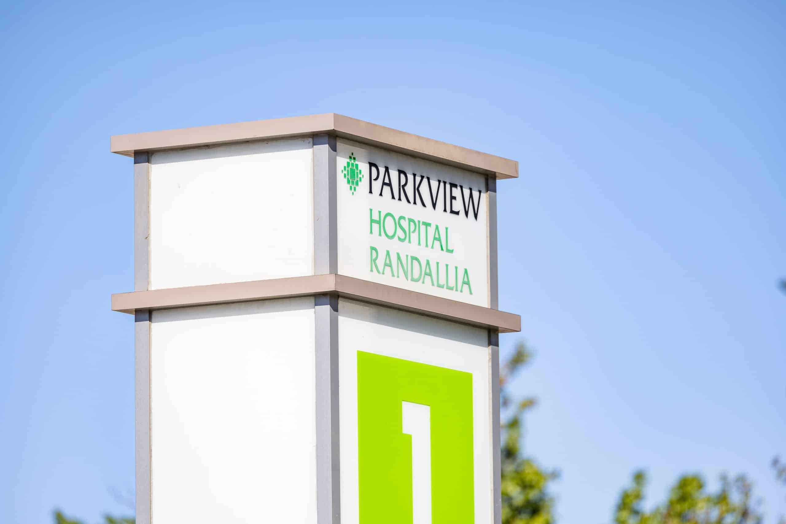 A tall, white, rectangle sign with black and green text reads, "Parkview Hospital Randallia."